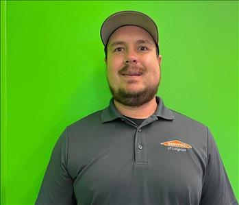man in a grey SERVPRO shirt standing in front of a green background. 