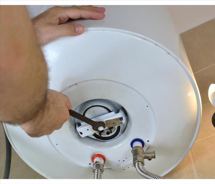 Man's hands unscrewing a threaded nut on a water heater with a wrench on a boiler.